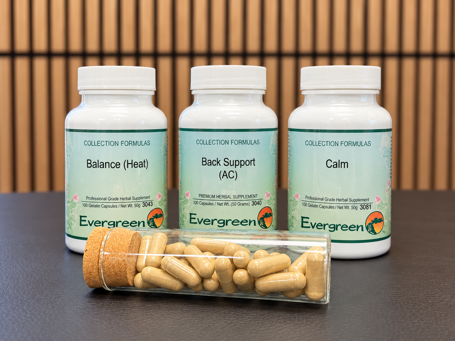 Evergreen herbal capsule bottles and a glass vial of capsules against warm walnut slats