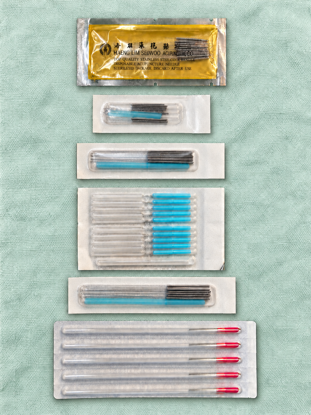 Assortment of packaged acupuncture needles with different lengths and handles on teal fabric